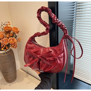 Detail of red pleated handbag featuring a shiny finish and decorative bow on cloud strap