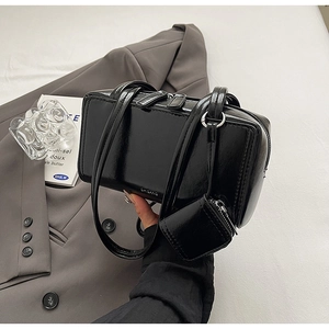Detail of black glossy square handbag with mini pouch accessory on a grey blazer suit