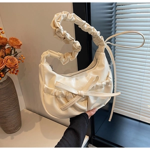 Detailed view of cream-white ruched bag with a bow accent and glossy leather finish