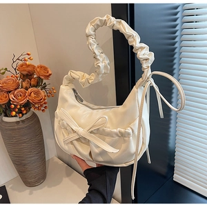Close-up of a cream pleated underarm bag featuring a large bow and a glossy finish
