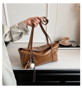 Close-up of caramel brown tote bag with OUR ABOR embossing and baseball charm accessory