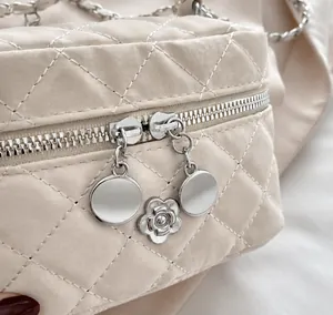 Detailed close-up of the smooth metal zipper and silver camellia flower pendant on the bag