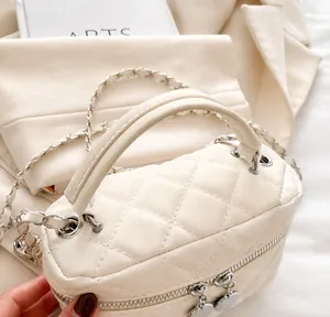 Detail of quilted creamy white mini handbag featuring silver chain strap and leather handle