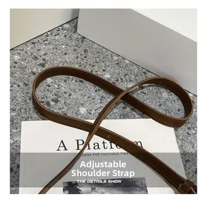 Détail de la bandoulière réglable en similicuir marron avec coutures fines sur livre