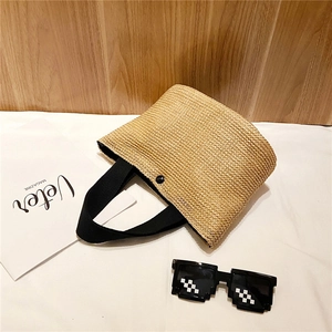 Detail of handwoven white straw tote bag with black strap and secure metal snap fastener