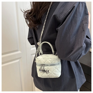 Detalle de bolso cilíndrico acolchado blanco con cadena y colgante de camelia
