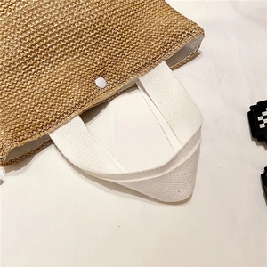 Close-up of handwoven straw tote with thick canvas handles and secure snap button closure