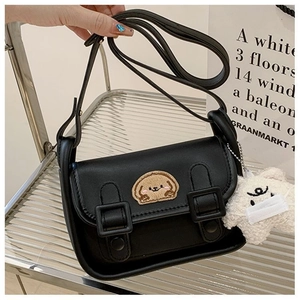 Détail d'un sac à bandoulière en cuir noir avec broderie chiot et breloque ours en peluche