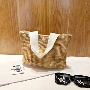 Close-up of handwoven straw tote with white canvas handles and metal snap button