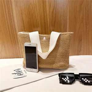 Detail of hand-woven straw tote bag with white canvas handles and snap button closure
