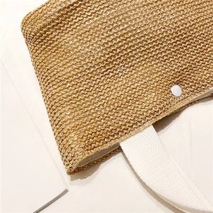 Detail of hand-woven straw tote bag showing tight texture and white fabric handle with snap