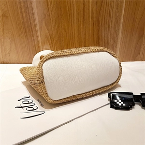 Detail of hand-woven straw bucket bag featuring a white textured leather base and handle