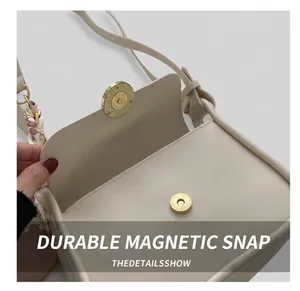 Close-up of cream leather shoulder bag featuring a magnetic gold clasp and silk scarf detail