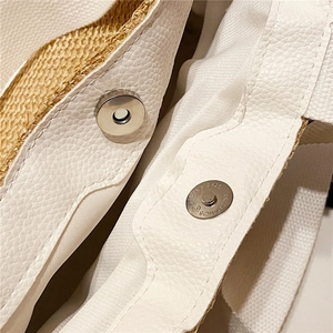 Close-up of silver magnetic buckle and white leather stitching on woven straw bag