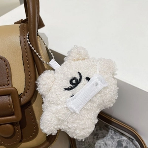 Détail d'un pendentif ours en peluche blanc avec chaîne argentée sur un sac à main