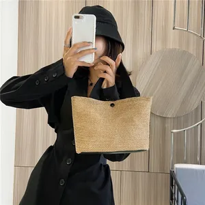 Detail of the woven texture and black strap on a beige straw tote bag for summer