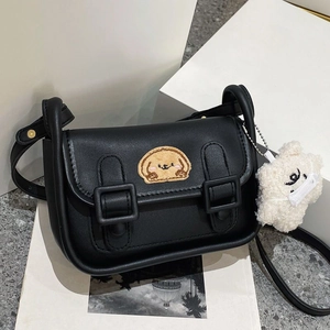 Détail d'un sac noir avec broderie de chien et pendentif d'ours en peluche doux