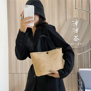 Detail of minimalist woven straw tote bag with black wide straps held by a model
