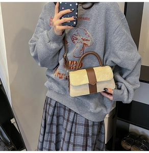 Detail van contrastkleurige stiksels op een beige en bruine crossbodytas met handvat