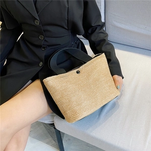 Detail of woven straw tote bag featuring black strap handles and metal snap closure