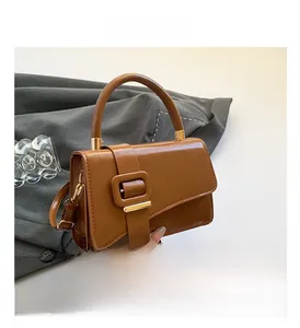 Detail of a brown glossy leather crossbody bag featuring a classic square buckle and top handle