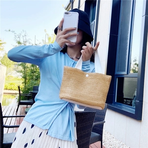 Detail view of woven straw tote bag with white fabric handles and button closure