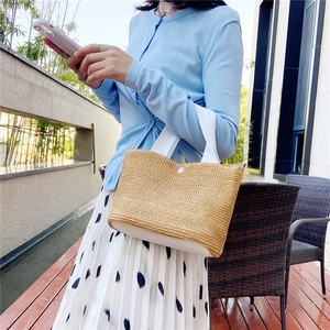 Detailed view of handmade woven straw tote bag with white leather handle and base