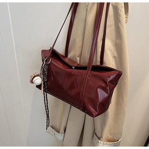 Detail of wine red patent leather tote bag with baseball charm on beige trench coat