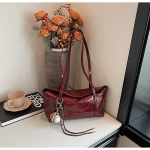 Detail of burgundy oil-wax leather shoulder bag with decorative baseball glove metal charm