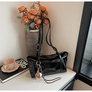 Detail of black glossy leather tote bag with unique shell charm and braided strap detail