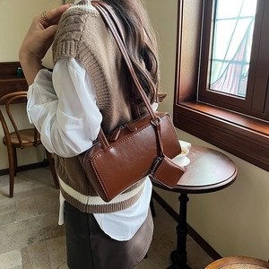 Chic brown leather shoulder bag with small accessory pouch in a retro indoor setting