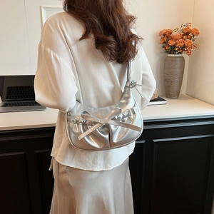 Silver metallic pleated crescent shoulder bag with bow detail worn by a model