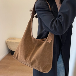 Sac fourre-tout en daim marron en forme de demi-lune porté avec une veste noire chic