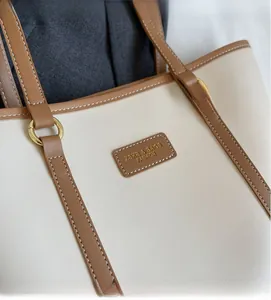 Close-up of cream and brown tote bag featuring golden rings and brand logo embossing