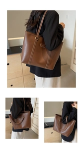 Detail of large brown leather tote bag with white contrast stitching and logo plaque