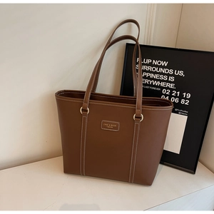 Detail shot of brown tote bag with white contrast stitching and minimalist leather logo