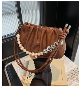 Detail of a brown pleated cloud bag with a large pearl handle and heart metal charms