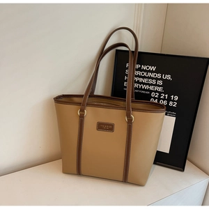 Close-up of brown faux leather tote bag showing the logo tag and gold metal hardware
