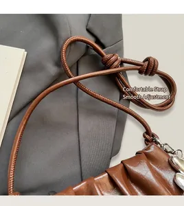 Detail of a brown ruched cloud bag showing the adjustable knot leather strap and metal chain