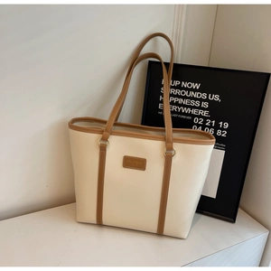 Detail of a large beige tote bag with brown leather trim and rectangular logo patch