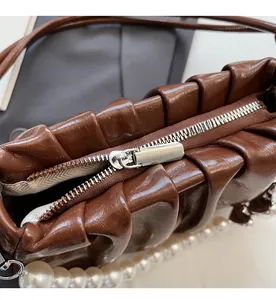 Close-up of smooth metal zipper and ruched leather detail on brown pearl bag
