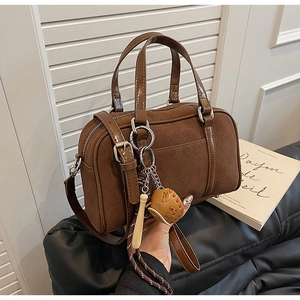 Vue détaillée d'un sac bowling en daim marron foncé avec poignées en cuir et breloques