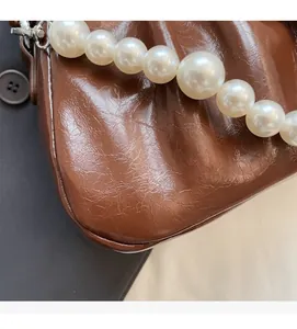 Close-up of brown pleated handbag featuring soft texture and large pearl handle detail