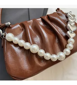 Close-up of brown pleated handbag featuring pearl strap and heart-shaped metal link chain