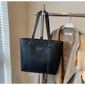 Detail of black tote bag with white contrast stitching and gold metal ring hardware