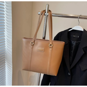 Macro detail of tan tote bag featuring contrasting white stitching and brand leather tag