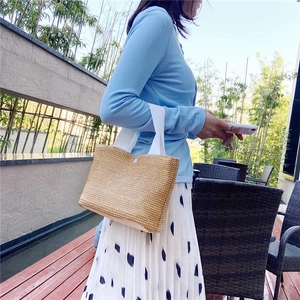 Detail of woven straw handbag with white fabric straps in a relaxed outdoor resort setting