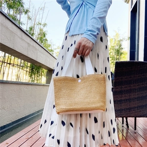 Detail of woven straw handbag featuring white webbing handles and button closure