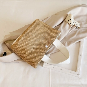 Close-up of woven straw handbag featuring white webbing handles and a snap closure