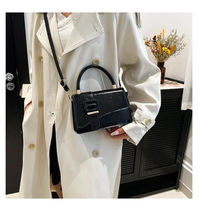 Detail of black patent leather crossbody bag with gold hardware worn on white trench coat